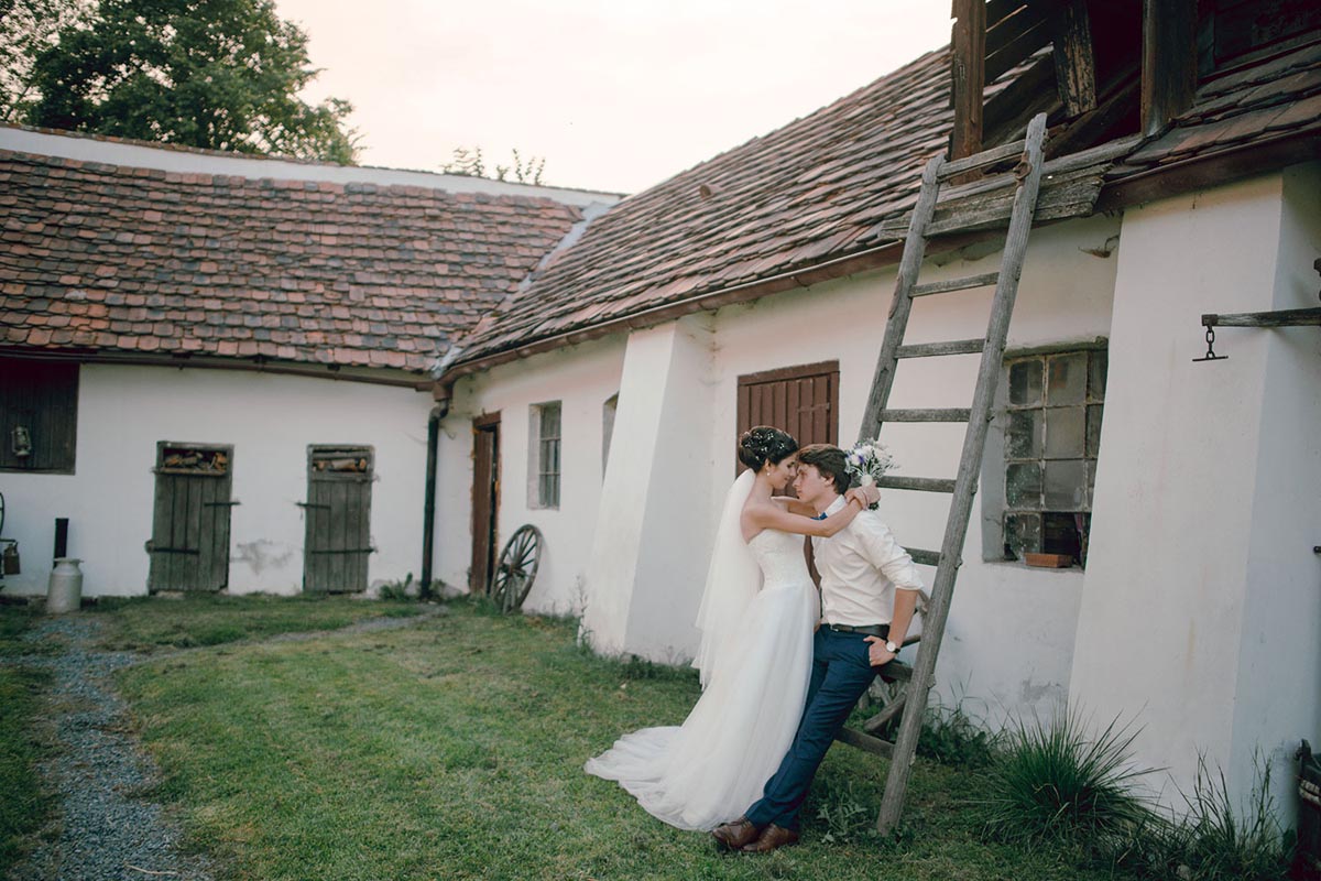 Bride and groom sit on an old ladder outside of the farmhouse