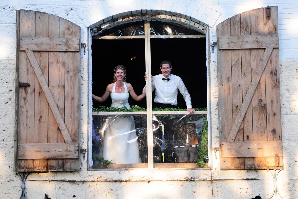Wedding venue setting depicting a happy bride and groom looking out of a farmhouse window