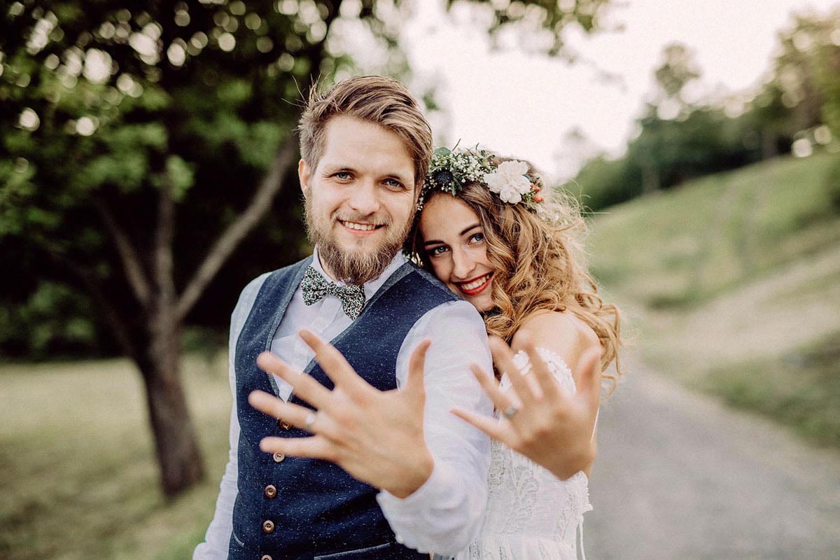 Happy bride and groom in green nature showing off new wedding rings